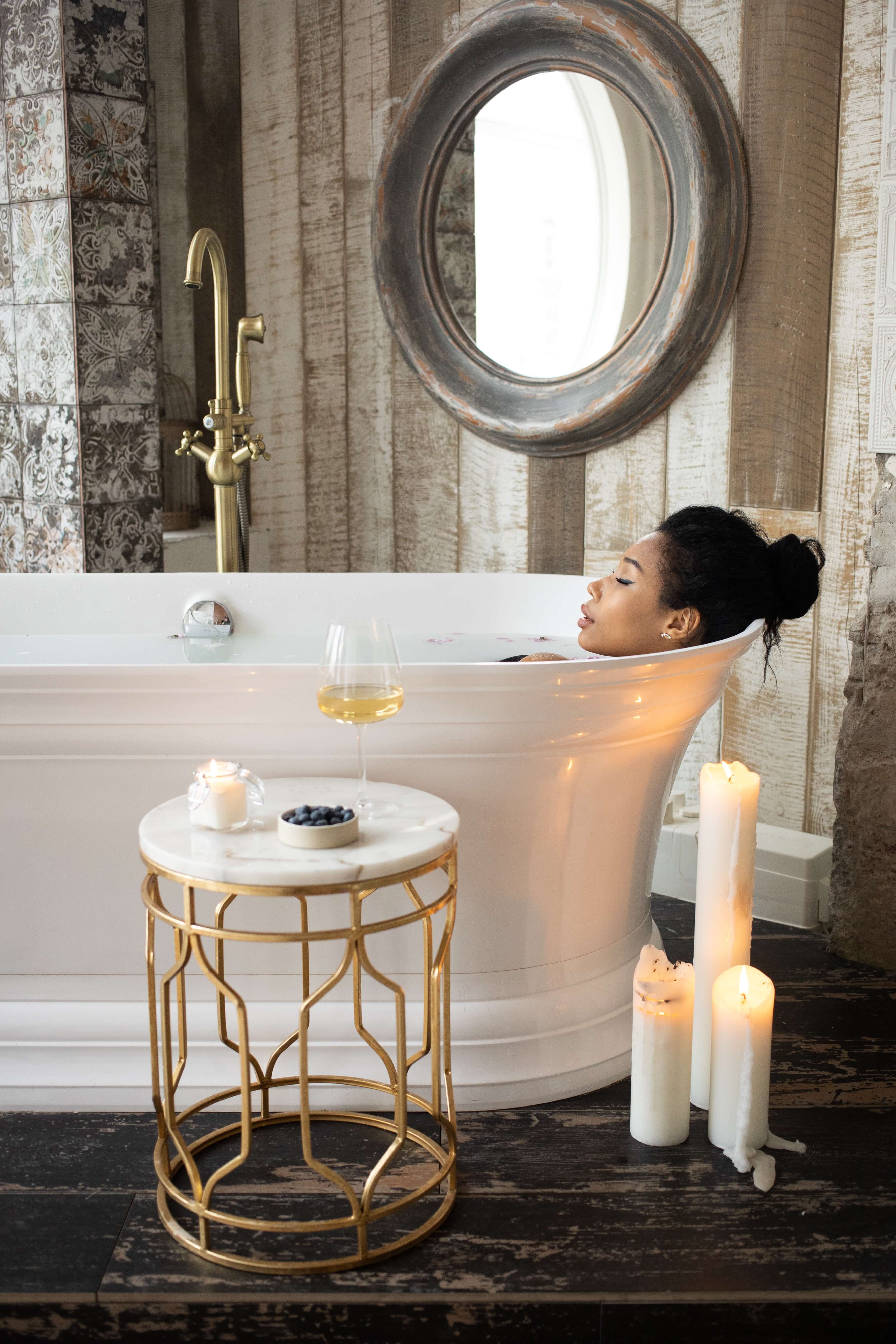 woman relaxing in a white bath tub with candles in the foreground